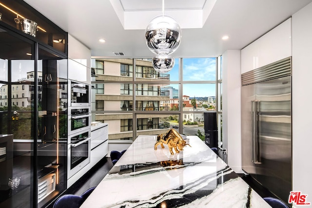 kitchen with white cabinets, hanging light fixtures, expansive windows, stainless steel appliances, and light stone countertops