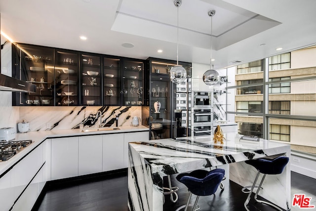 kitchen featuring extractor fan, a raised ceiling, pendant lighting, stainless steel gas stovetop, and white cabinets