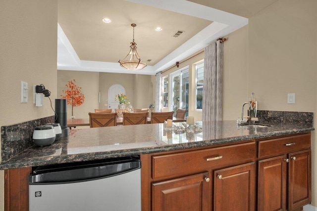 kitchen featuring a tray ceiling, dark stone countertops, sink, and stainless steel dishwasher