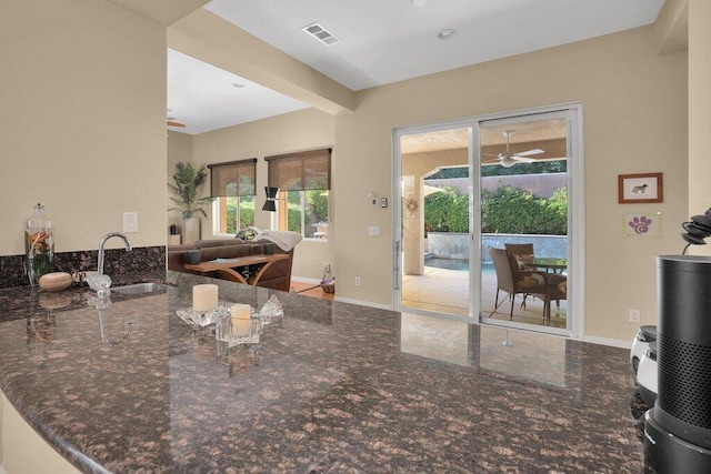 kitchen with sink, ceiling fan, dark stone countertops, beam ceiling, and kitchen peninsula