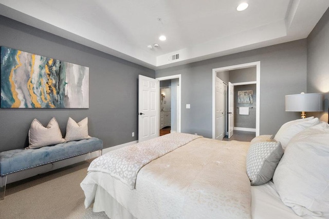 bedroom featuring ensuite bathroom, a raised ceiling, and carpet flooring