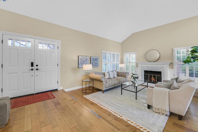 living room featuring plenty of natural light, light hardwood / wood-style floors, vaulted ceiling, and a brick fireplace