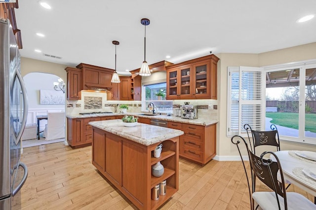 kitchen with light stone countertops, appliances with stainless steel finishes, pendant lighting, light hardwood / wood-style flooring, and a kitchen island