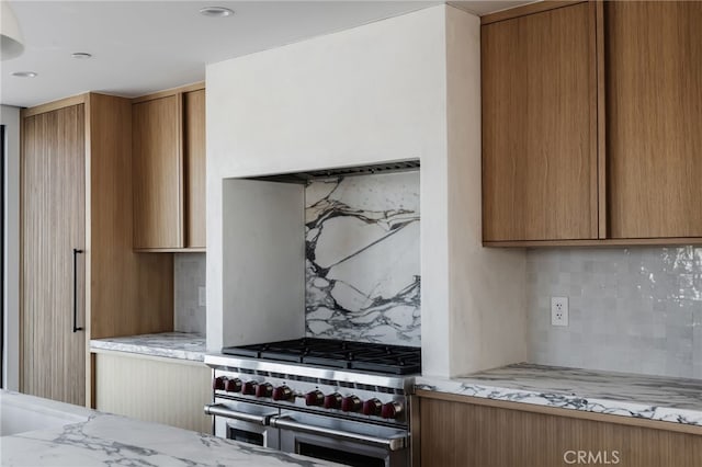 kitchen with range with two ovens, light stone countertops, and backsplash