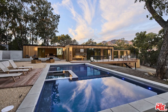 pool at dusk featuring an outdoor living space, an in ground hot tub, a deck with mountain view, and a patio area