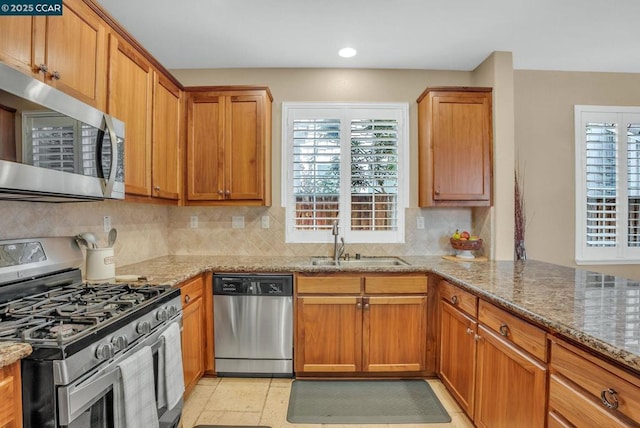 kitchen with light stone countertops, sink, stainless steel appliances, kitchen peninsula, and decorative backsplash