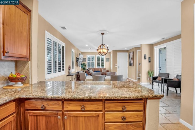 kitchen featuring light stone counters, kitchen peninsula, a chandelier, decorative light fixtures, and decorative backsplash