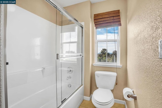 bathroom featuring tile patterned flooring, combined bath / shower with glass door, and toilet