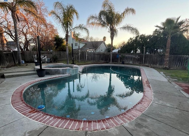 pool at dusk featuring a patio area and an in ground hot tub