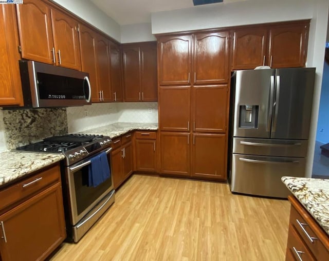 kitchen with light wood-type flooring, appliances with stainless steel finishes, backsplash, and light stone counters