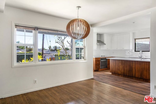 kitchen with stainless steel oven, pendant lighting, dark hardwood / wood-style flooring, wall chimney range hood, and backsplash