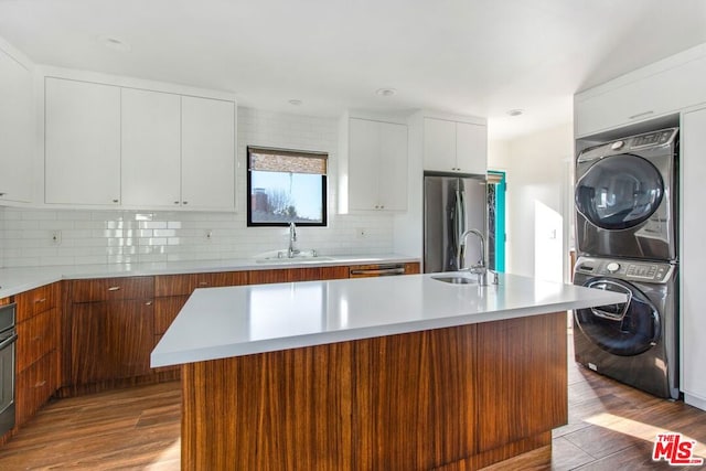 kitchen with sink, stacked washer and clothes dryer, a kitchen island with sink, and appliances with stainless steel finishes