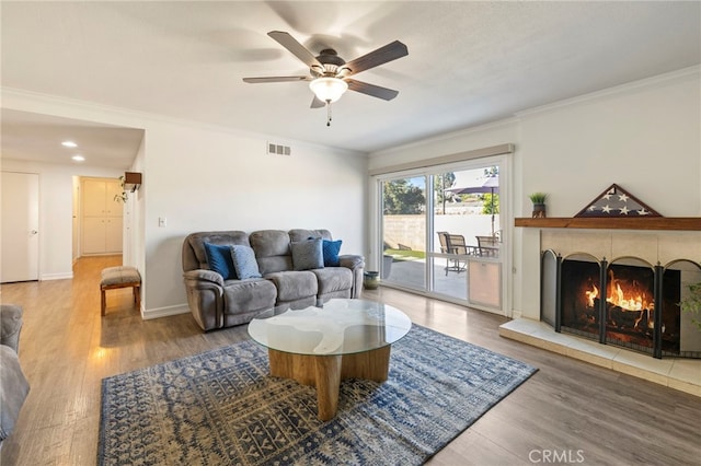 living room with a tile fireplace, ceiling fan, hardwood / wood-style flooring, and crown molding