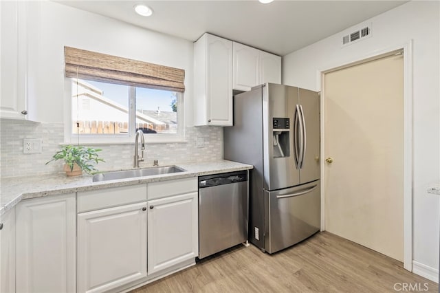 kitchen with light stone countertops, stainless steel appliances, light wood-type flooring, white cabinetry, and sink