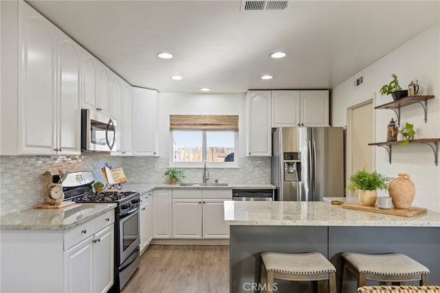 kitchen with stainless steel appliances, sink, white cabinetry, a breakfast bar area, and light stone countertops