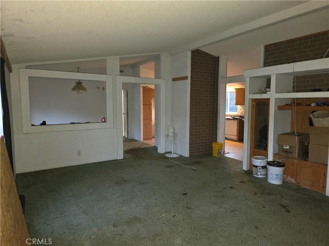 unfurnished living room with a textured ceiling, vaulted ceiling, and brick wall