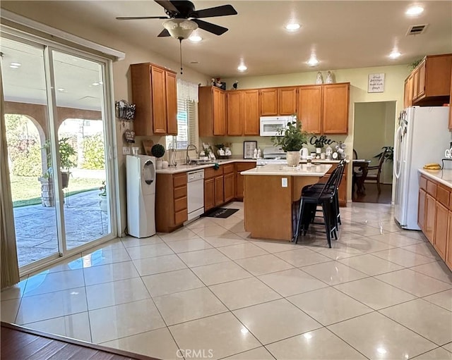 kitchen featuring white appliances, light tile patterned floors, ceiling fan, a kitchen bar, and a kitchen island