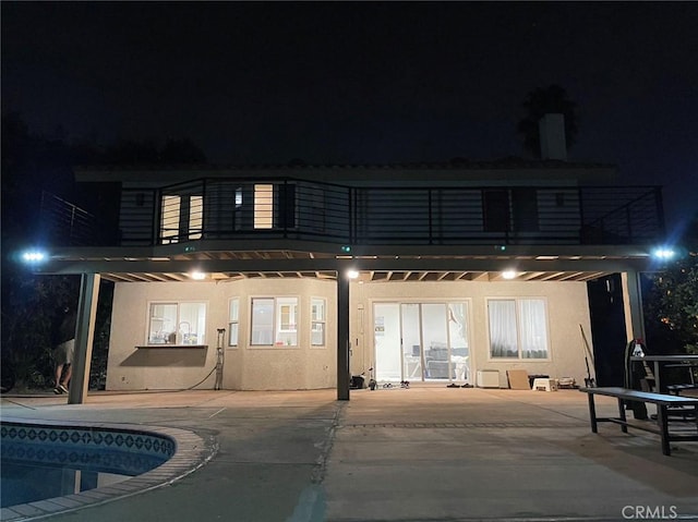 back house at night featuring a patio and a balcony