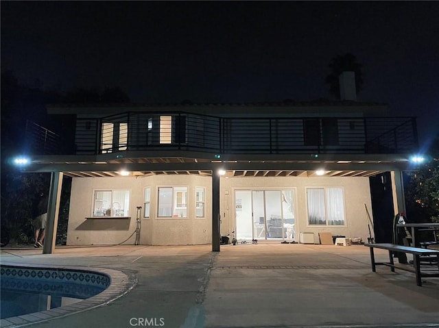 back of house at twilight featuring an outdoor pool, a patio, a balcony, and stucco siding