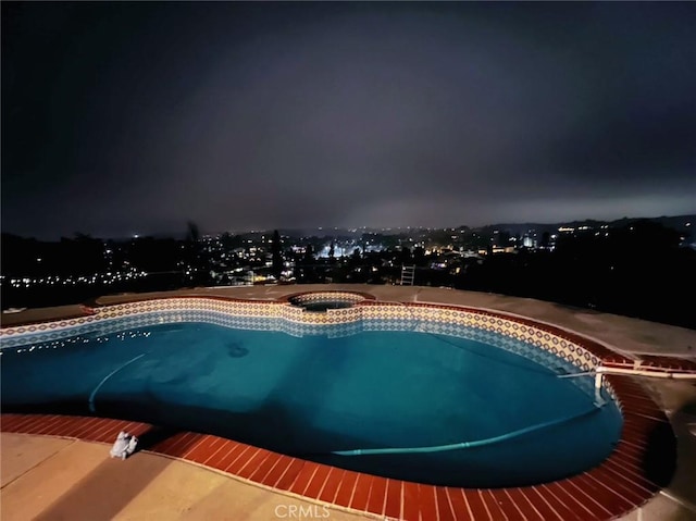 pool at night featuring an outdoor pool and an in ground hot tub