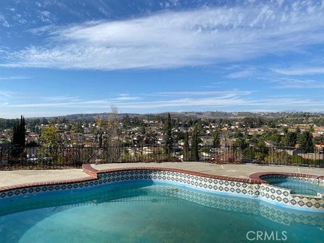 view of pool featuring a pool with connected hot tub and fence