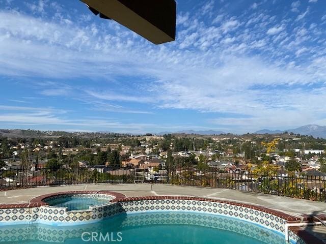 view of swimming pool with a mountain view, a pool with connected hot tub, and fence