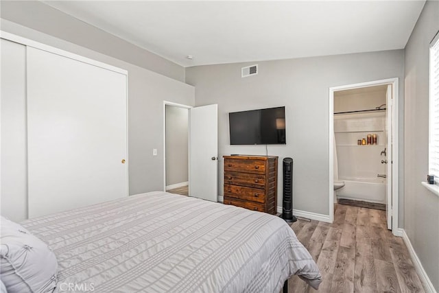 bedroom with ensuite bath, a closet, lofted ceiling, and light wood-type flooring