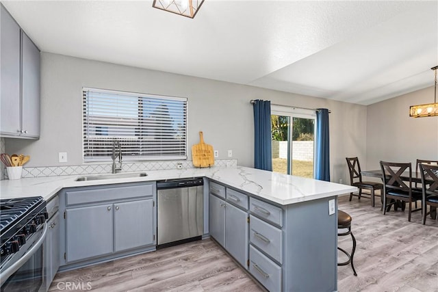 kitchen featuring kitchen peninsula, appliances with stainless steel finishes, sink, decorative light fixtures, and a breakfast bar area