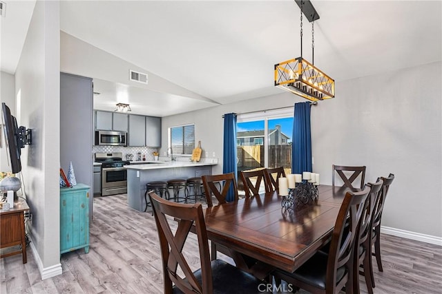 dining space with light hardwood / wood-style flooring, lofted ceiling, and a notable chandelier