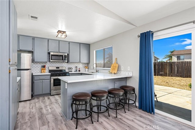 kitchen featuring gray cabinetry, stainless steel appliances, kitchen peninsula, vaulted ceiling, and a breakfast bar