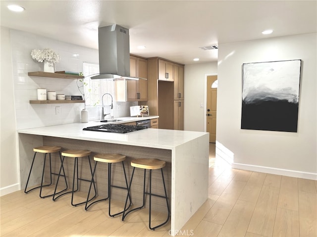 kitchen with island range hood, sink, a breakfast bar area, kitchen peninsula, and light wood-type flooring