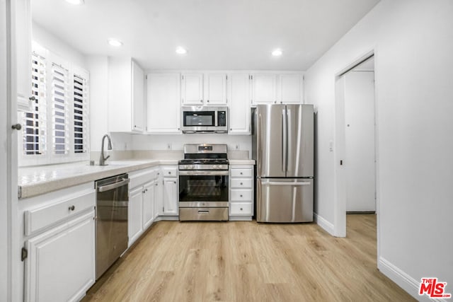 kitchen with appliances with stainless steel finishes, light hardwood / wood-style flooring, white cabinetry, and sink