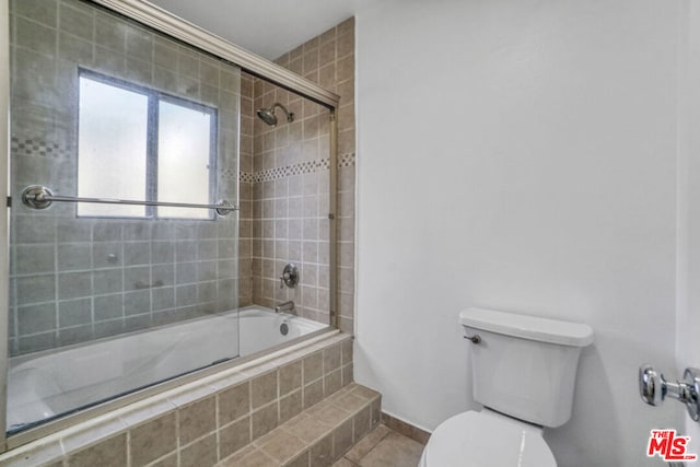 bathroom with tile patterned floors, combined bath / shower with glass door, and toilet