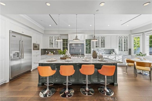 kitchen featuring white cabinetry, a large island, light stone counters, built in appliances, and decorative light fixtures