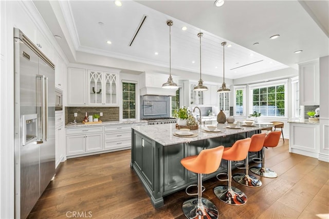 kitchen featuring a kitchen bar, light stone counters, stainless steel appliances, a center island with sink, and white cabinetry