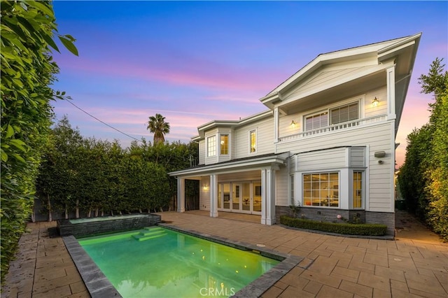 back house at dusk featuring a balcony, a patio, and french doors