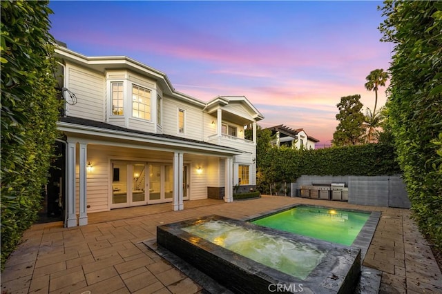 back house at dusk with a pool with hot tub, a patio area, and a balcony