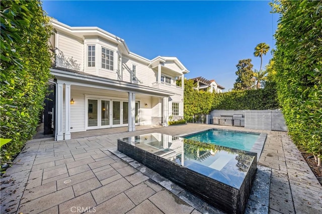 rear view of house featuring a swimming pool with hot tub, a patio, and an outdoor kitchen