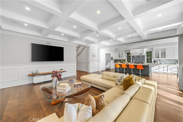 living room featuring beamed ceiling, ornamental molding, light wood-type flooring, and coffered ceiling