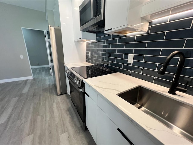 kitchen with appliances with stainless steel finishes, sink, tasteful backsplash, white cabinetry, and light stone countertops