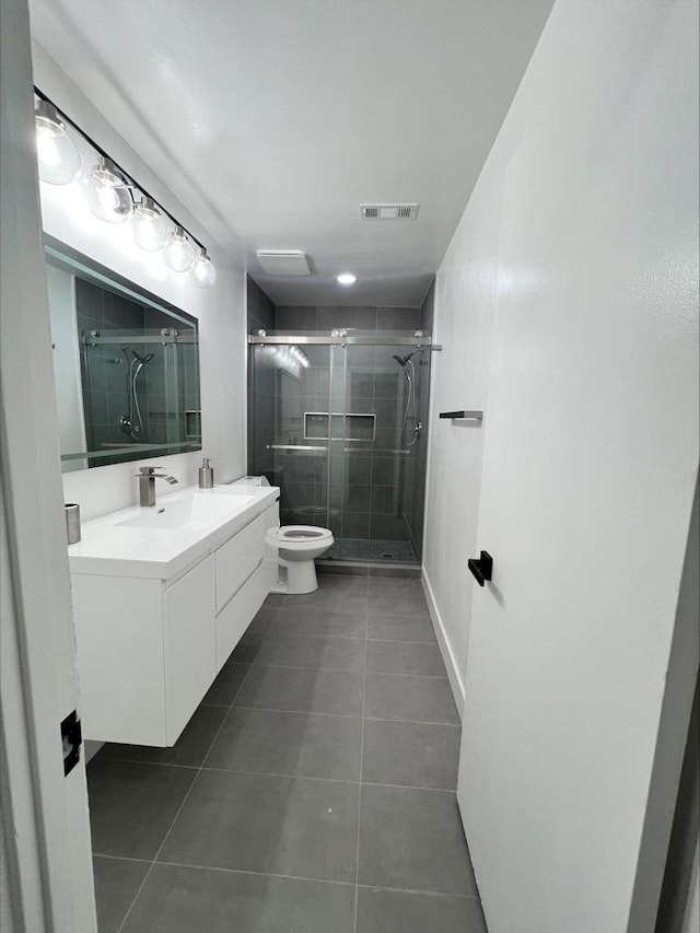 bathroom featuring a shower with shower door, toilet, vanity, and tile patterned flooring