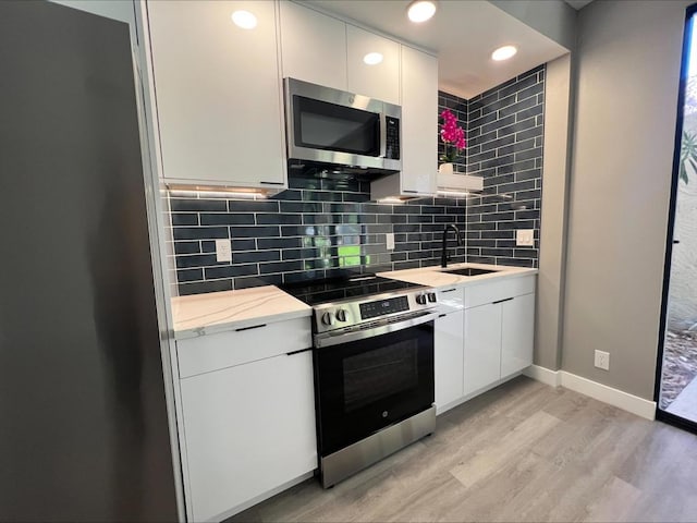 kitchen featuring white cabinets, stainless steel appliances, decorative backsplash, sink, and light wood-type flooring