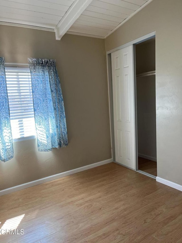 unfurnished bedroom featuring beam ceiling, a closet, wooden ceiling, and wood-type flooring