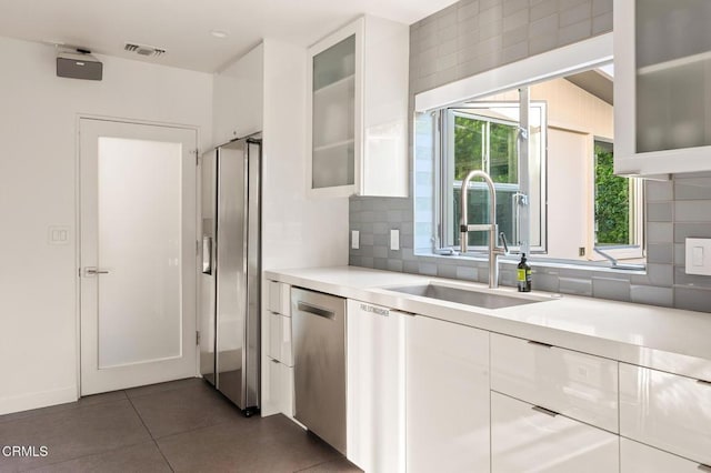 kitchen with dishwasher, white cabinets, sink, dark tile patterned floors, and tasteful backsplash