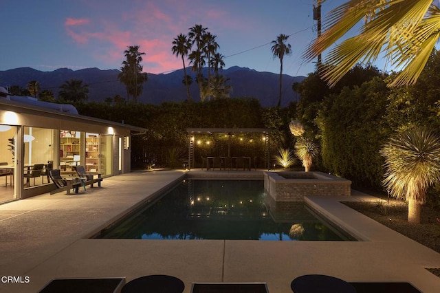 pool at dusk featuring an in ground hot tub, a mountain view, and a patio area