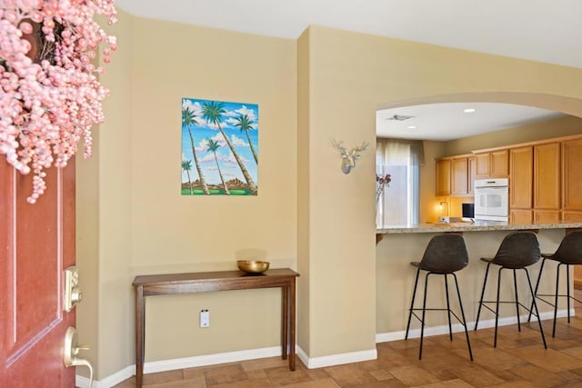 kitchen featuring white oven, light stone countertops, and a kitchen breakfast bar