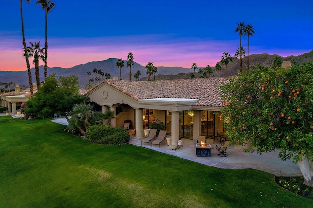 back house at dusk featuring a fire pit, a mountain view, a patio area, and a yard