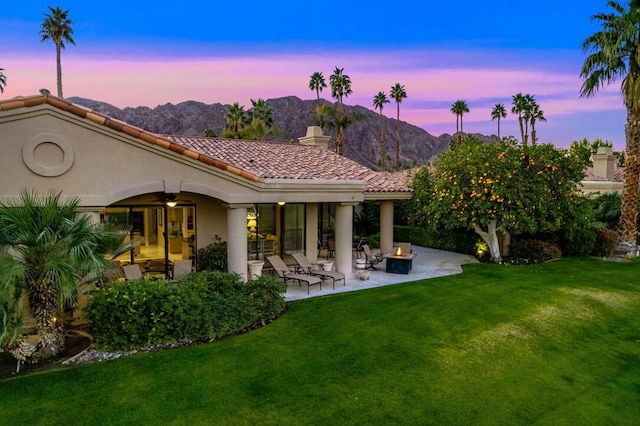 back house at dusk featuring a patio, a mountain view, a yard, and ceiling fan