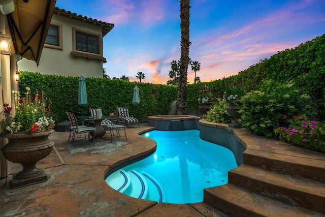 pool at dusk featuring an in ground hot tub and a patio