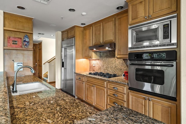 kitchen with backsplash, built in appliances, sink, and dark stone counters